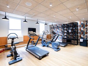 Une salle de sport équipée de tapis de course, de vélos elliptiques et d’un mur orné d’un motif abstrait aux couleurs vives.