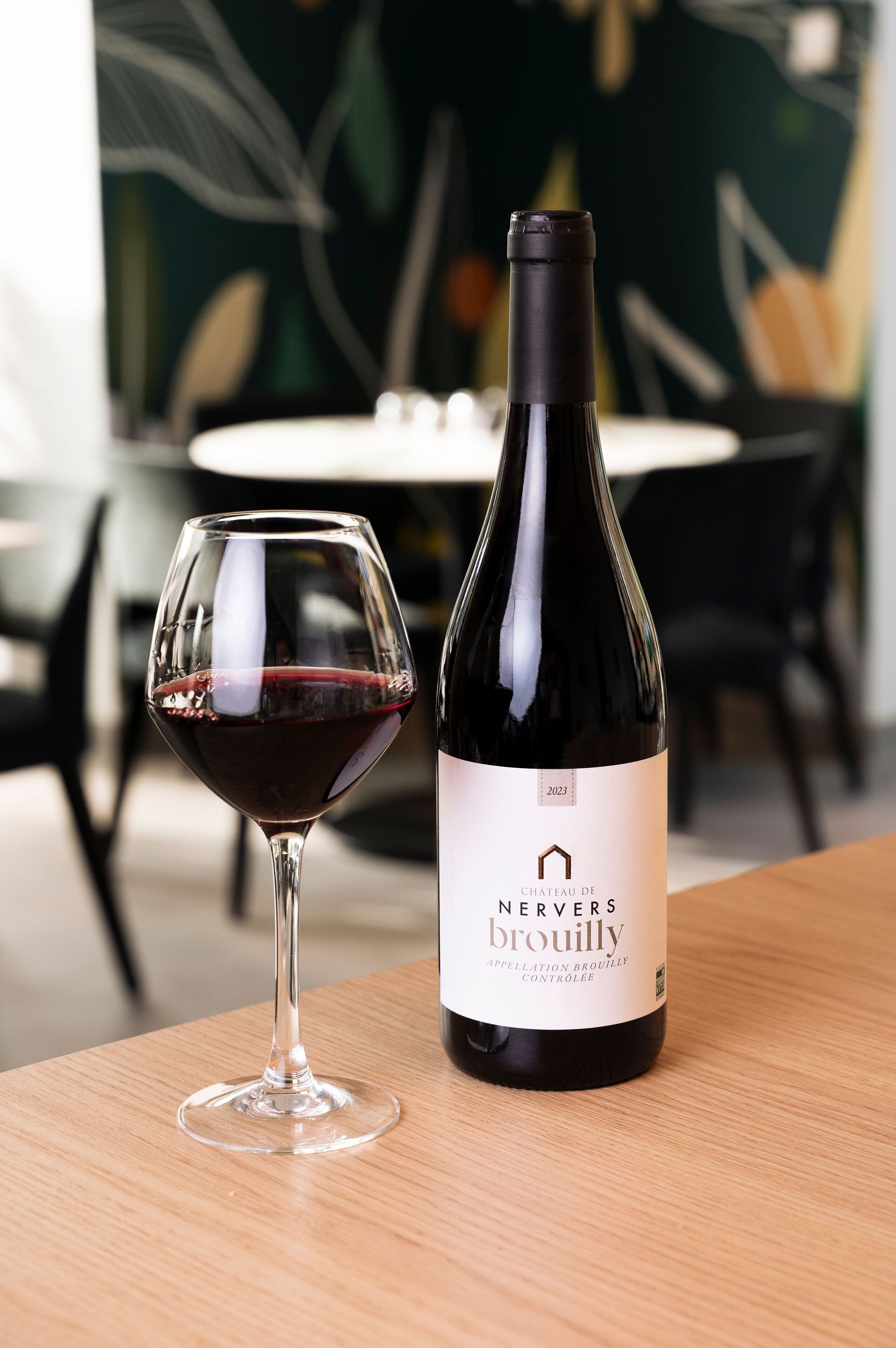 Une bouteille de vin Nervers Brouilly et un verre de vin rouge sur une table en bois.