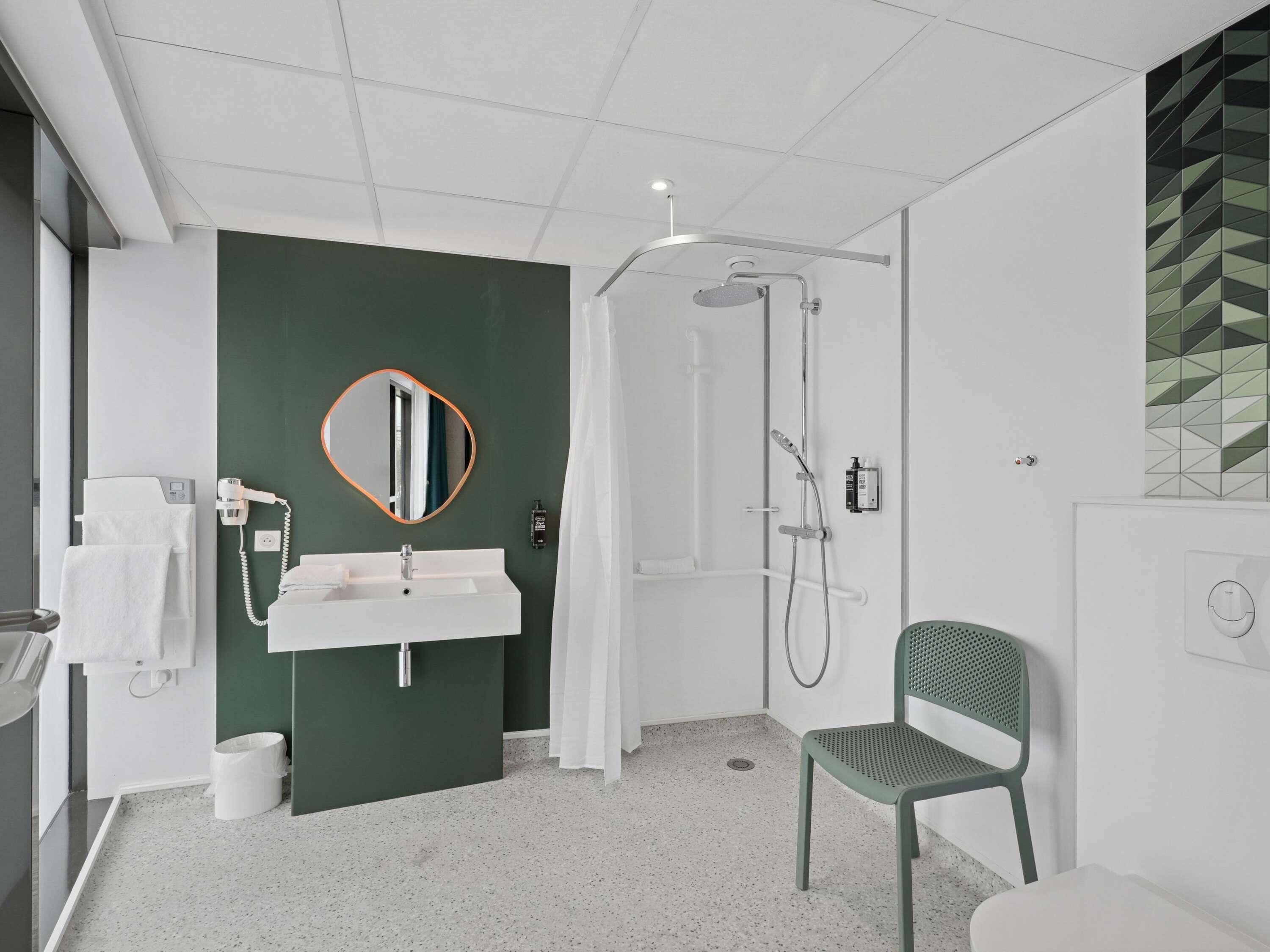 A modern bathroom with a white sink, green wall, and a shower area.