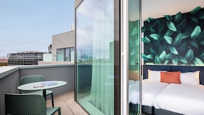 A modern hotel room with a city view, a balcony with seating, and a large leaf-patterned wall. - Ibis Styles Bezons Paris La Défense (Opening March 2024) (Bezons)