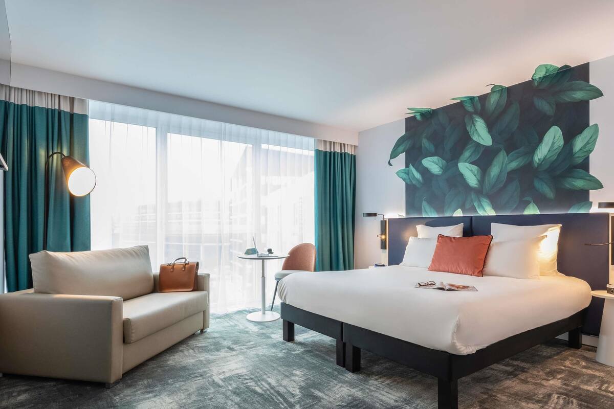 A hotel room with a bed, a sofa, a desk, a chair, and a large wall mural.