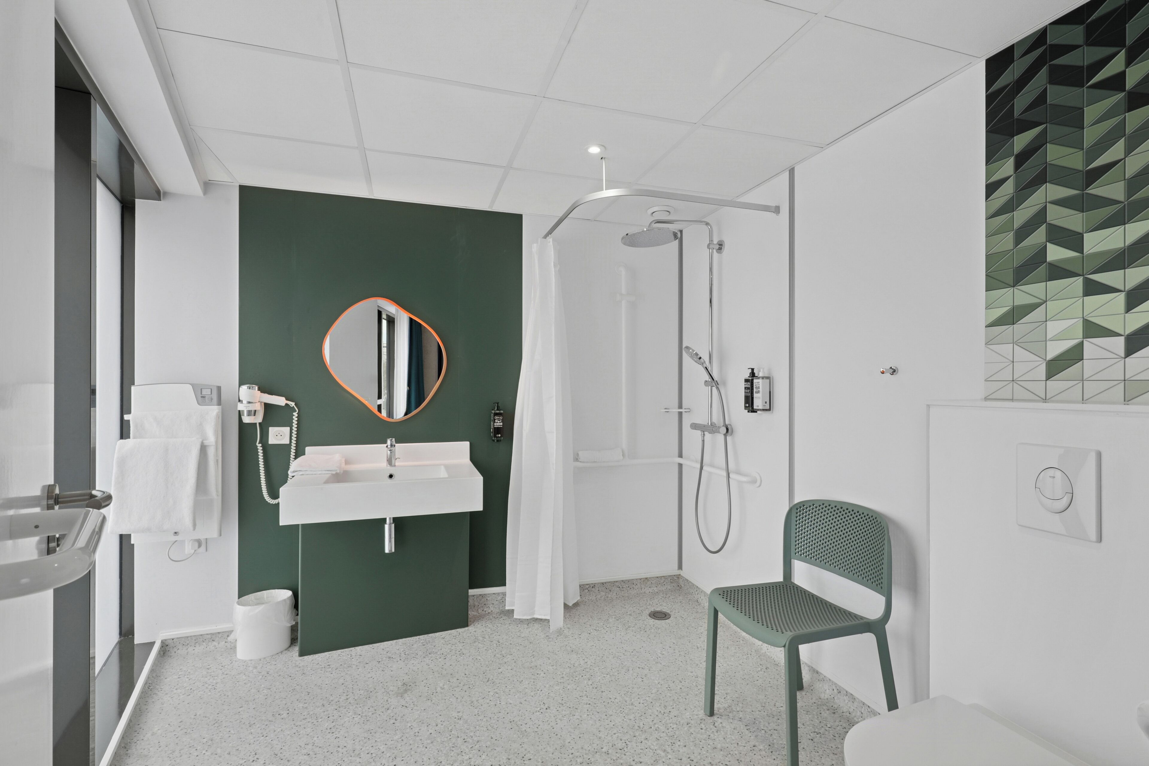 A modern bathroom with a white sink, green wall, and a shower area.