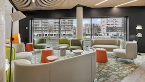 A modern lounge area with seating, a large window offering a city view, and a wooden ceiling with integrated lighting. - Ibis Styles Bezons Paris La Défense (Opening March 2024) (Bezons)