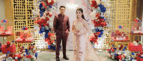 A couple standing in front of a decorative backdrop with floral arrangements and traditional Chinese symbols.