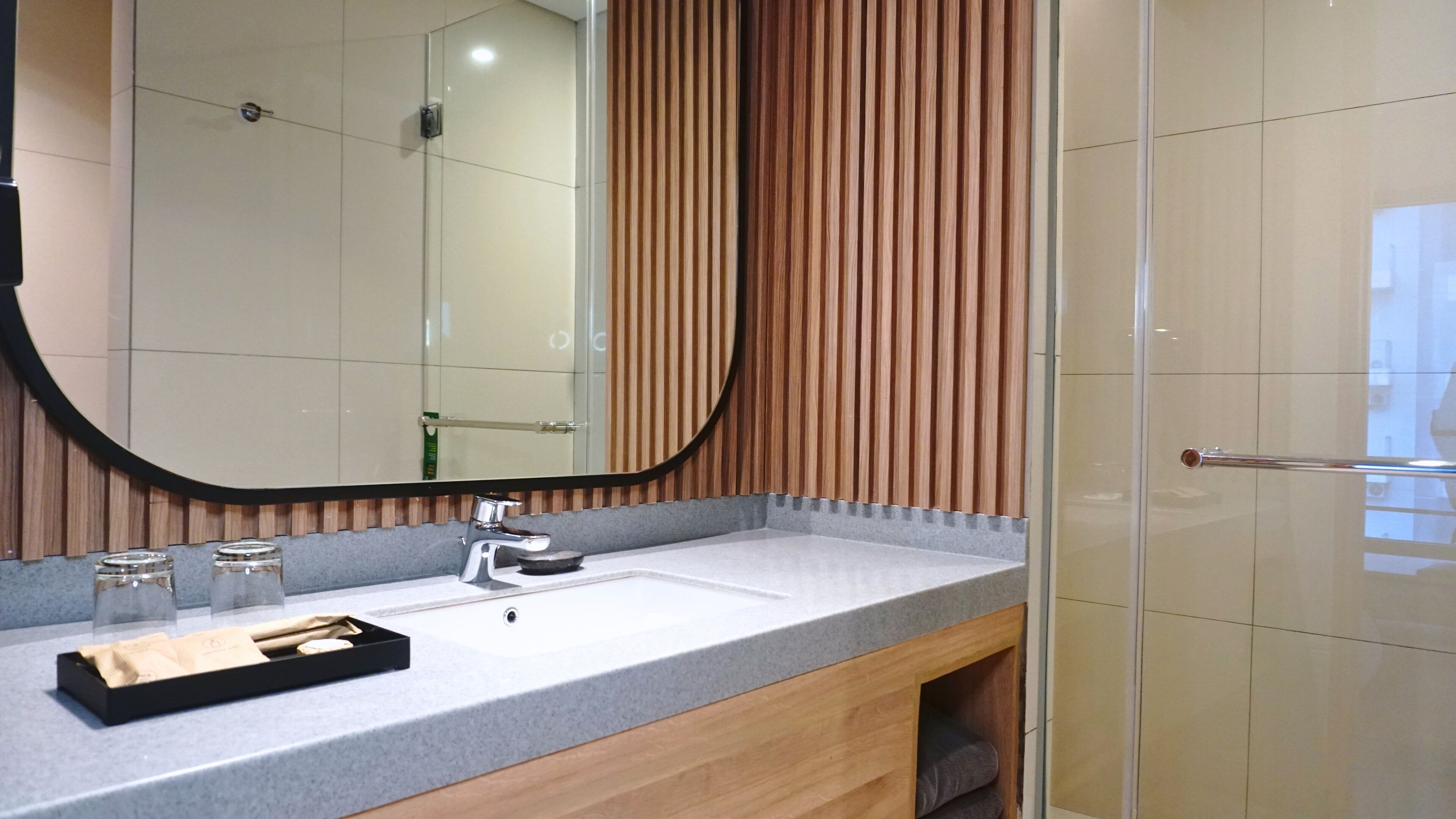 A modern bathroom with a large mirror, a sink, and a wooden panel wall.