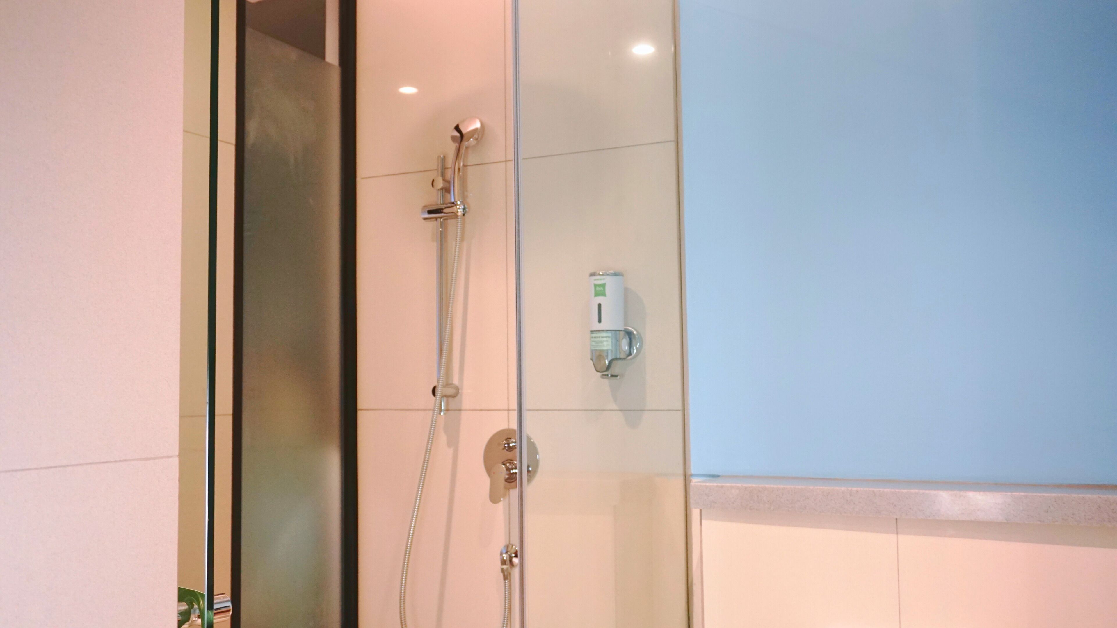 A glass-enclosed shower with a handheld showerhead and a wall-mounted faucet.