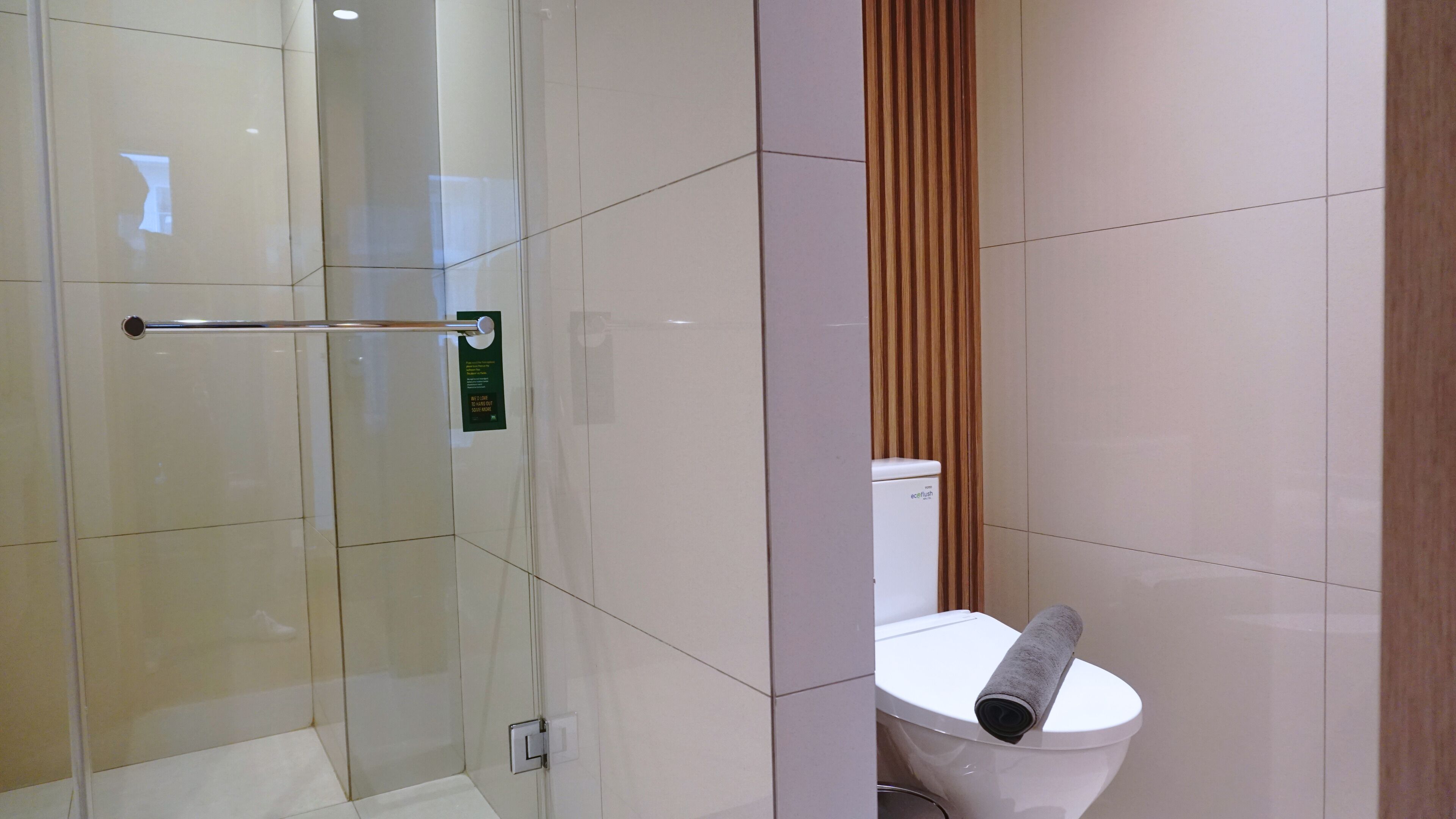 Un baño moderno con cabina de ducha de vidrio, inodoro con una toalla en el asiento y pared de paneles de madera.