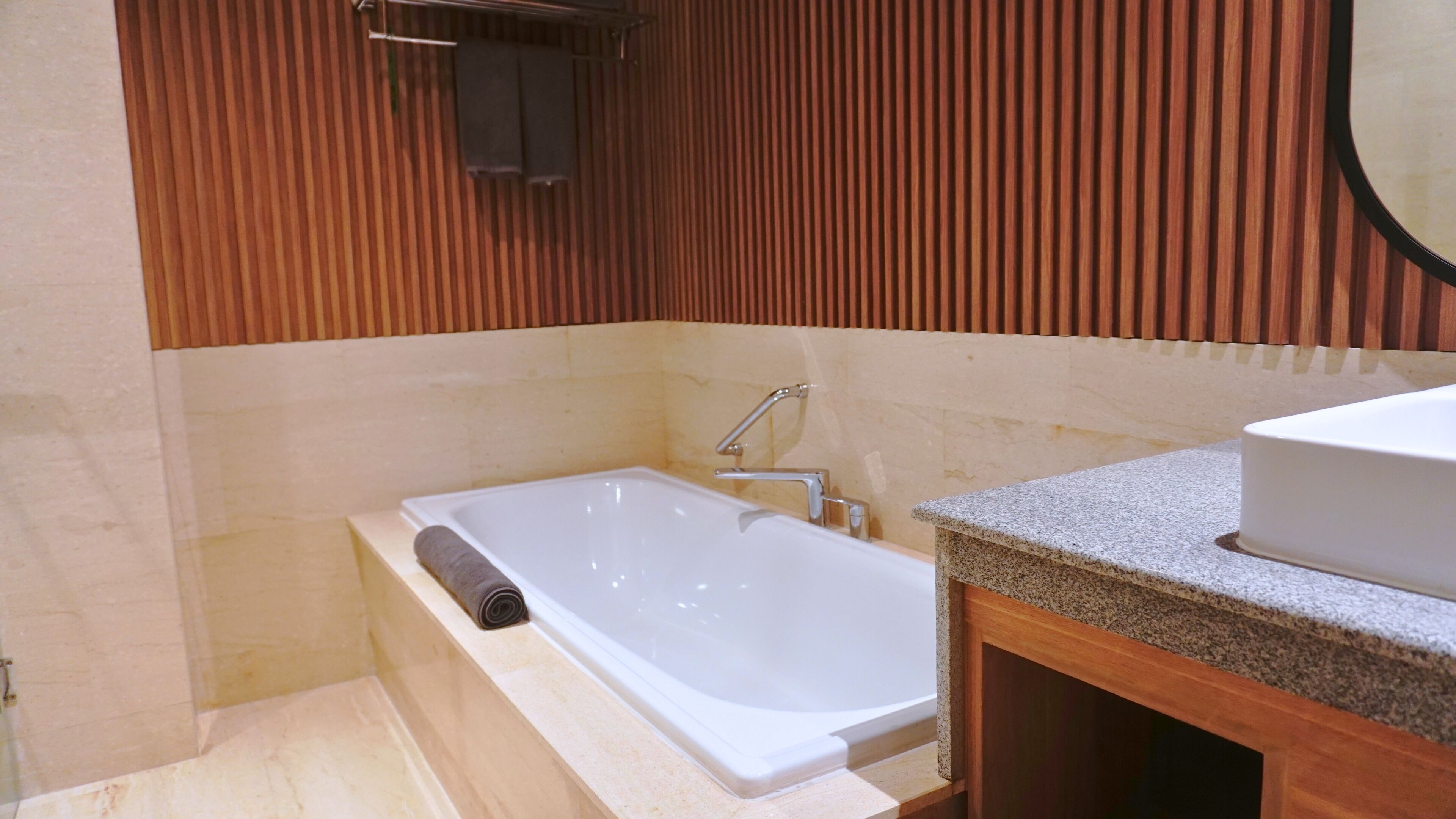 A modern bathroom with a freestanding bathtub, a granite countertop, and a wooden panel wall.