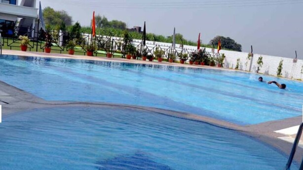 Una piscina con agua azul cristalina, rodeada de plantas en macetas y banderas.