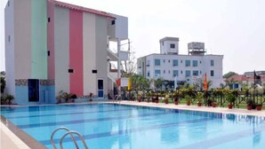 Una piscina con escalera metálica, rodeada por un edificio de fachada multicolor y otro edificio blanco en el fondo.