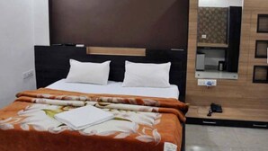 Habitación de hotel con cama, cabecero de madera, espejo y una mesita con un teléfono.