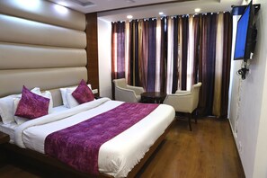 Una habitación de hotel con una cama grande, un escritorio, dos sillas y un televisor montado en la pared.