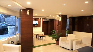 Un vestíbulo moderno con sofás blancos, una mesa de centro, un televisor montado en la pared y una planta en maceta.