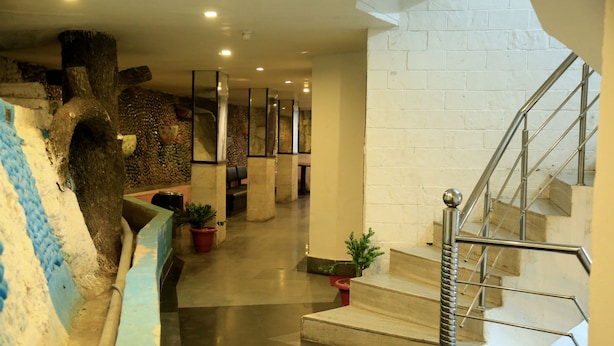 Un vestíbulo de hotel con una escalera, un árbol decorativo y una zona de estar con plantas en macetas.