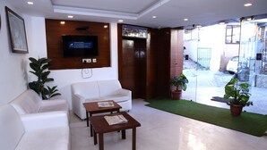 Un hall moderno con un sofá blanco, dos mesas de madera, un televisor montado y plantas en macetas.