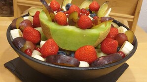 A fruit bowl with a variety of fruits including strawberries, grapes, and bananas, placed on a black tray. - Stadthotel im Kolpinghaus  (Werne)