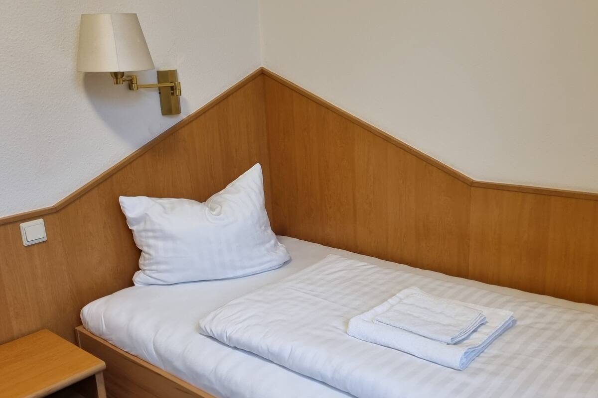 A single bed with a wooden headboard, a bedside table, a nightstand, and a wall-mounted lamp.