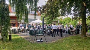 An outdoor gathering with tables and chairs, surrounded by trees and a building with a red roof. - Stadthotel im Kolpinghaus  (Werne)