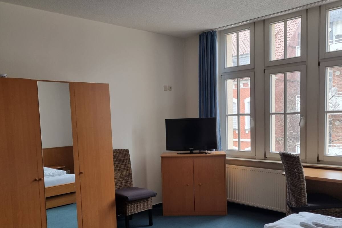 A hotel room with a bed, a TV, a chair, a wardrobe, and a window with a view of buildings.