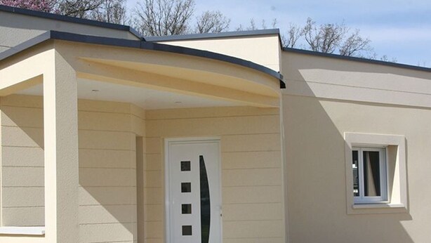 Ein Gebäude mit einer beige farbenen Fassade, einer weißen Tür mit einem besonderen Design und einem kleinen Fenster zur Rechten.