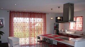 Eine moderne Küche mit einer zentralen Kochinsel, Barhocker, einem Essbereich mit einer Couch und einem großen Fenster mit Vorhängen.