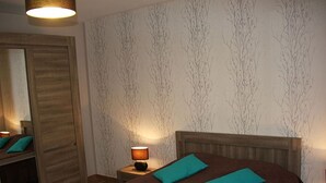 Ein Schlafzimmer mit einem Holz-Kopfteil, einem Bett mit türkisfarbenen Kissen, einem Nachttisch mit Lampe und einem Spiegel an der Wand.