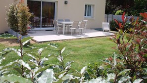 Eine moderne Außenpatio mit Tisch und Stühlen, umgeben von einem gepflegten Rasen und verschiedenen Pflanzen.
