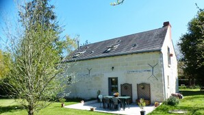 A stone building with a sloped roof, a patio with outdoor furniture, and a small garden area.