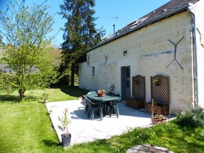 Un bâtiment rustique en pierre, doté d’une terrasse, de sièges en plein air et de plantes en pot.