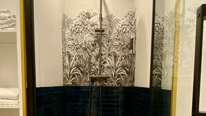 Eine gläserne Duschkabine mit Regendusche, dunkelblauen Fliesen und einem dekorativen Blütenpaneel an der Wand.