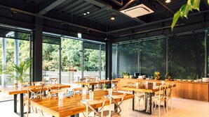 A spacious indoor dining area with wooden tables and chairs, large windows offering a view of greenery outside. - HOTEL BEGINS (Keelung)