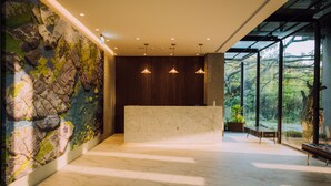 A reception area with a marble reception desk, a stone wall mural, and a view of greenery through large windows. - HOTEL BEGINS (Keelung)