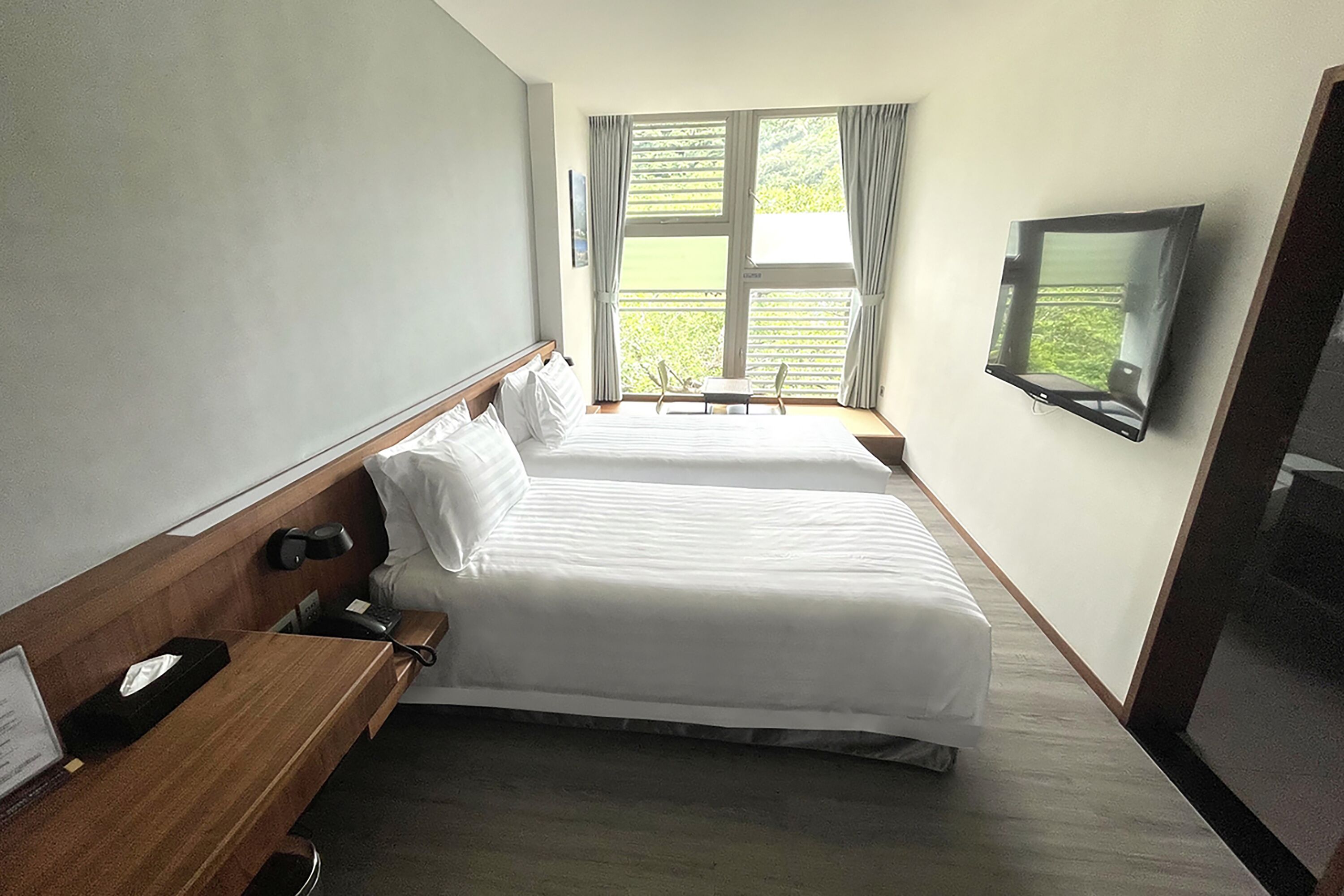 Habitación de hotel con dos camas, un escritorio con teléfono, televisor montado en la pared y ventana con cortinas.