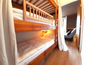 A bunk bed with a wooden frame, a lower bunk with a mattress, and a headboard with a light fixture. - Cozy studio for 4 with equipped kitchenette, St-Lary-Soulan (Saint-Lary-Soulan)