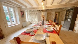 A dining room with a long wooden table set for a meal, stone walls, and a rustic ceiling. - Charming Cottage with Private Heated Pool, Fitness Room, Game Room, Near Rillé Lake (Rillé)