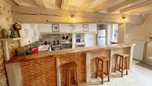 A kitchen with a brick accent wall, wooden bar stools, and a white countertop. - Charming Cottage with Private Heated Pool, Fitness Room, Game Room, Near Rillé Lake (Rillé)