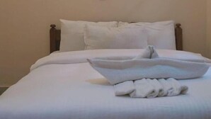Cama bem arrumada com lençóis brancos e uma toalha dobrada sobre ela.