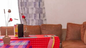 Uma sala de estar com toalha xadrez vermelha e azul, um sofá marrom e uma cadeira com moldura dourada.