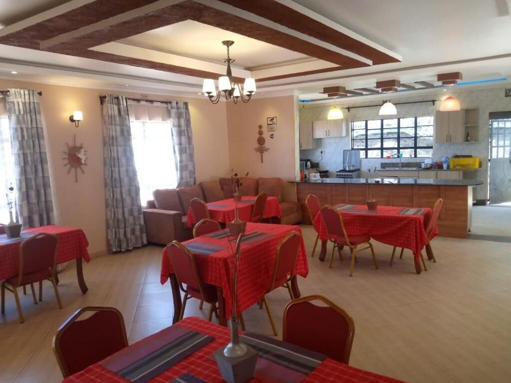 Un comedor con mesas y sillas, una cocina al fondo y una araña.