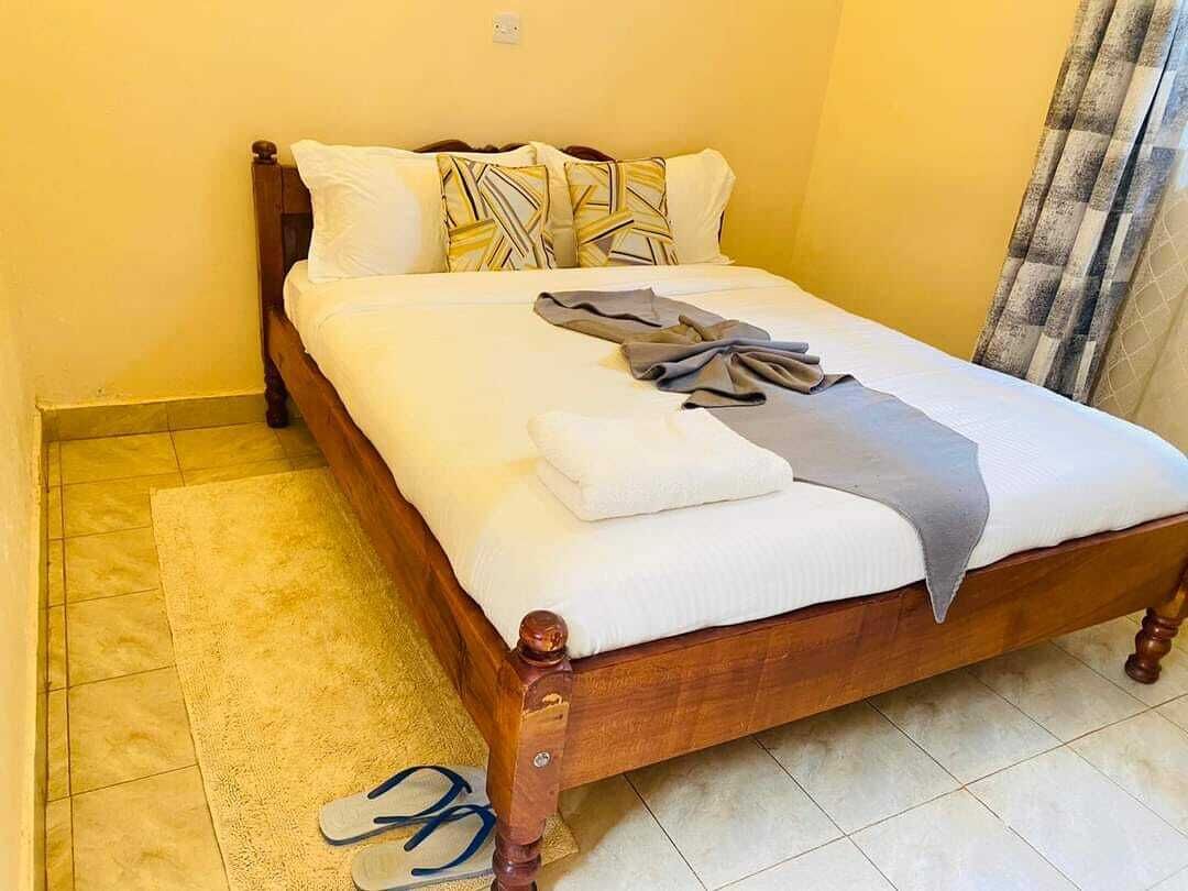 A neatly made bed with a white comforter and pillows, a gray blanket, and a folded towel.