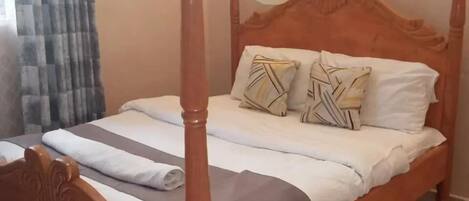 Un lit à baldaquin, deux oreillers à motifs géométriques et une couverture à rayures.