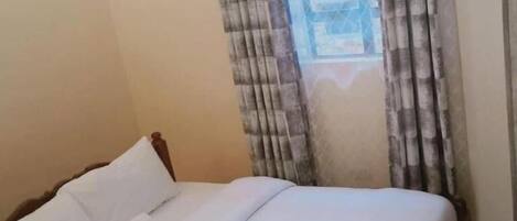 Una cama bien hecha en una habitación con una ventana cubierta por cortinas.