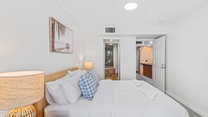 A hotel room with a bed, a lamp, a checkered pillow, a painting, and a bathroom visible through an open door. - Zanzibar 505 amazing beachfront resort apartment withm pool , spa and access to gym (Mooloolaba)
