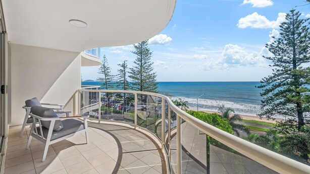 A balcony with a view of the ocean and beach, featuring a chair and a table. - Zanzibar 505 amazing beachfront resort apartment withm pool , spa and access to gym (Mooloolaba)