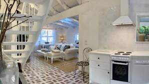 Une cuisine moderne avec des meubles blancs, une cuisinière et un lave-vaisselle. On y trouve un coin repas avec une table et des chaises blanches, ainsi qu’un salon avec un canapé et une lampe.