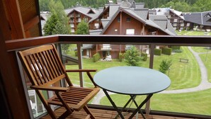 A balcony with a wooden chair and a small table, overlooking a well-maintained lawn and a row of buildings. - Studio for 4 at Hameaux du Lay with parking (Les Contamines-Montjoie)