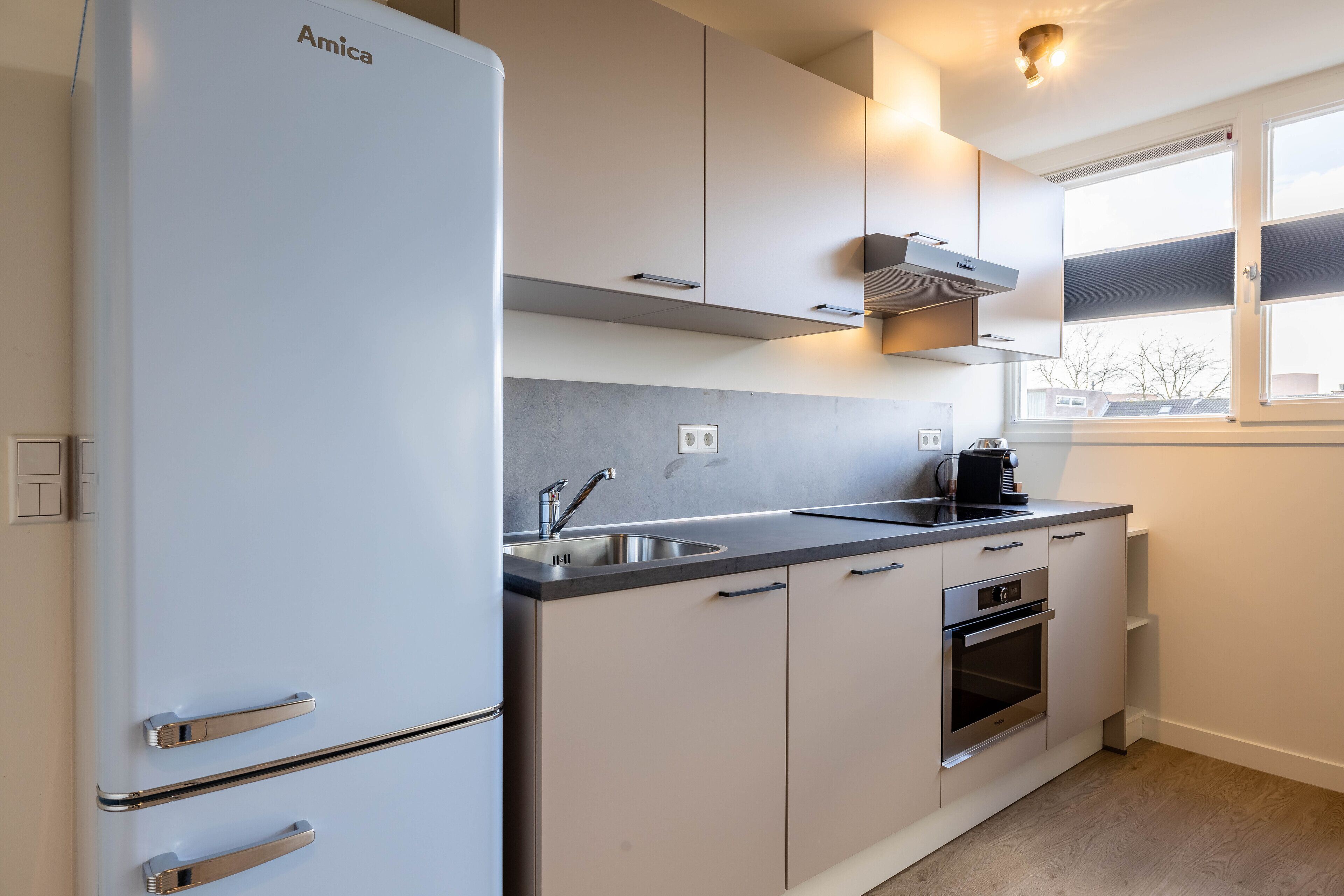 A modern kitchen with a white refrigerator, stainless steel oven, and a window providing natural light.