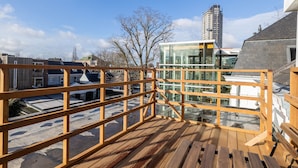 Une terrasse sur le toit, dotée de rampes en bois, d’une structure vitrée et offrant une vue sur les bâtiments environnants.
