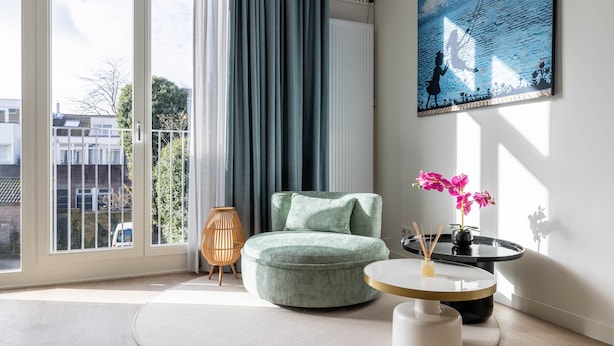 Un salon moderne avec un canapé vert rond, une table basse ronde et un tableau accroché au mur.