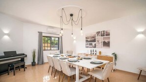 A dining area with a piano, a chandelier, and a table set for four. - Spacious House | Terrace & Pool by Host Wise (Lagoa)